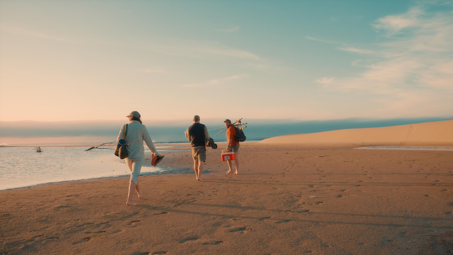 Guests walking barefoot along an empty beach beside the dunes at golden hour
