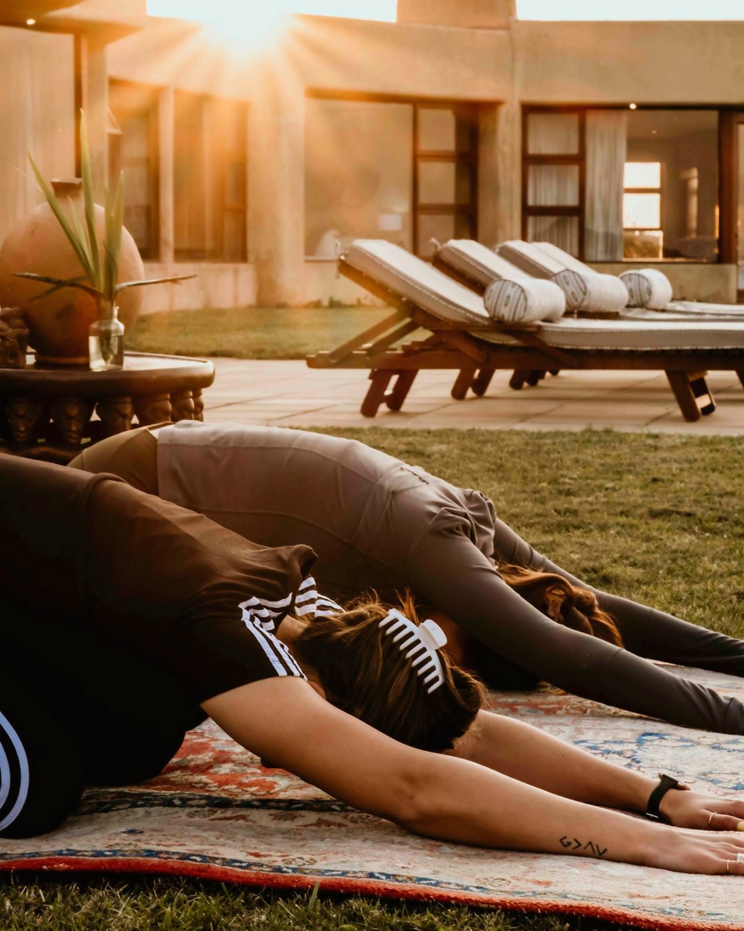 Two guests stretching on rugs on the villa lawn at golden hour, with the patio and loungers beyond