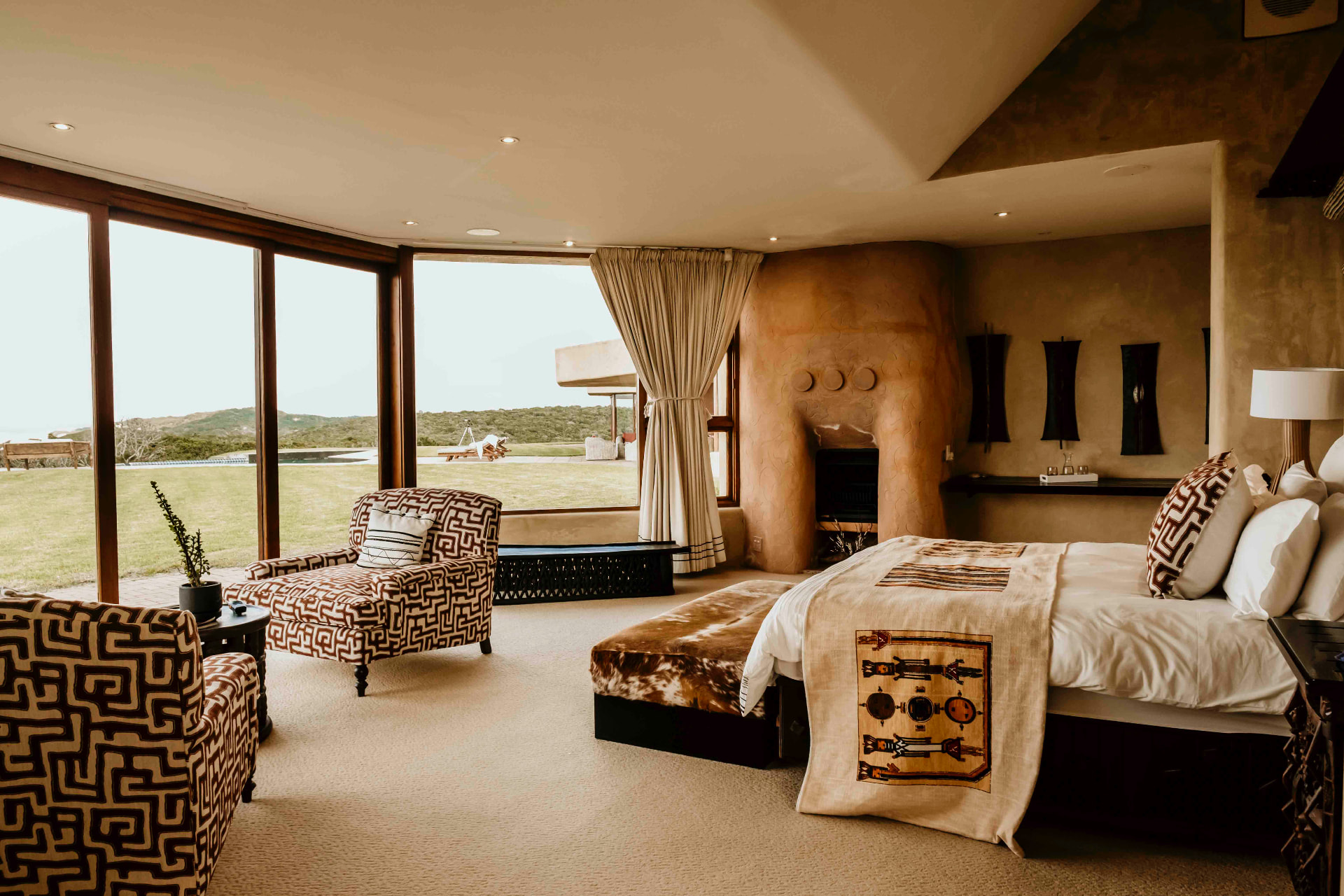 The primary suite — sculpted plaster fireplace, African textiles and floor-to-ceiling windows onto the lawn