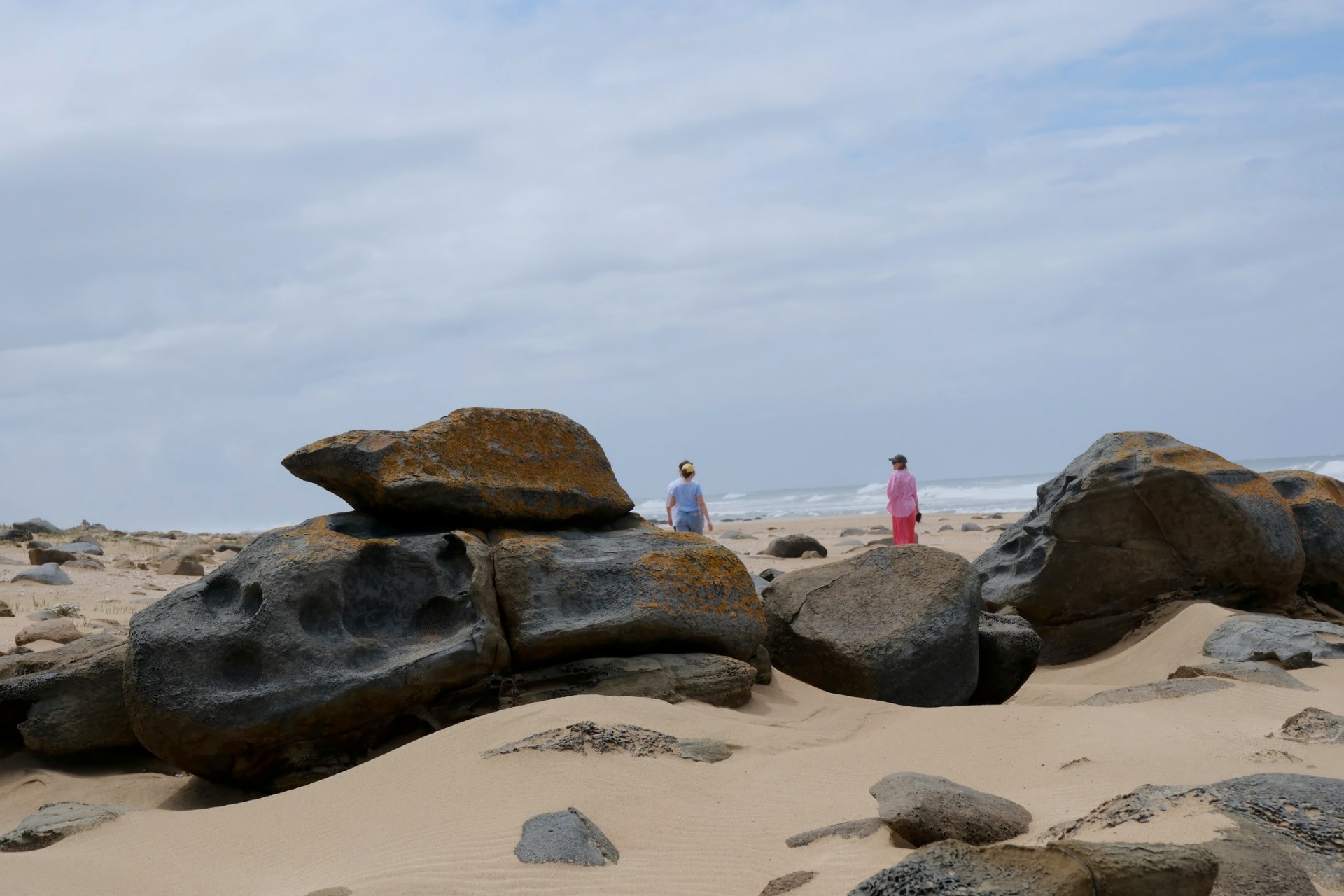 Weathered boulders on the sand at the foot of the dunes, the ocean beyond
