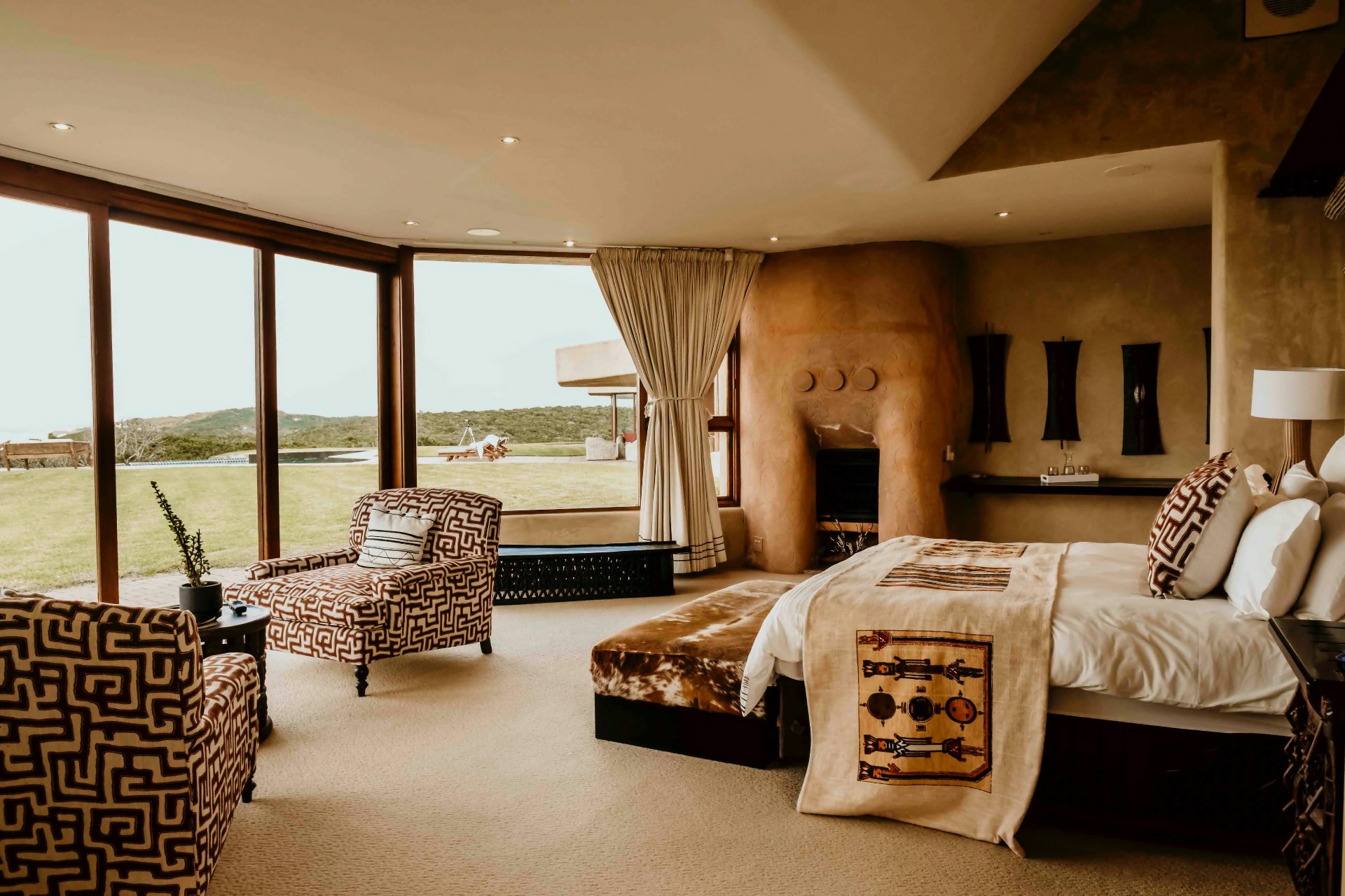 The primary suite — sculpted plaster fireplace, African textiles and floor-to-ceiling windows onto the lawn