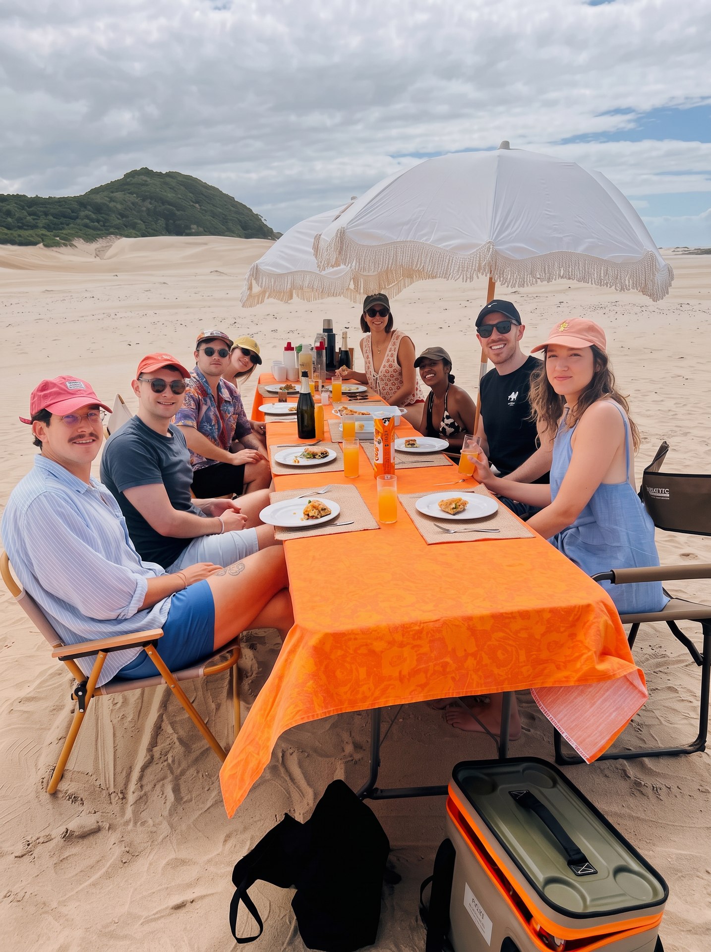 A long table laid for dinner on the sand beneath fringed beach umbrellas